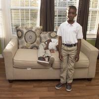 Two young brothers posing for a picture, one standnig up the other laying on a couch